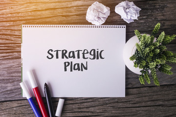 Strategic Plan word with Notepad and green plant on wooden background.