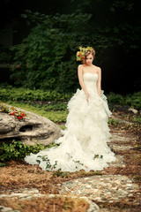 Fashionable bride with an artful look in a lush white dress is standing on a dark nature.