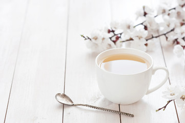 Tasse blanche de thé chaud avec des fleurs de ressort sur un fond en bois clair