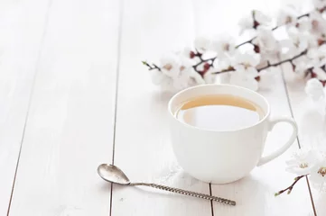 Photo sur Plexiglas Theé Tasse blanche de thé chaud avec des fleurs de ressort sur un fond en bois clair