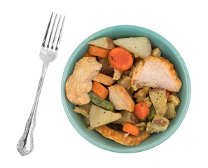 Bowl of turkey breast with stuffing and vegetables plus a fork to the side isolated on a white background.