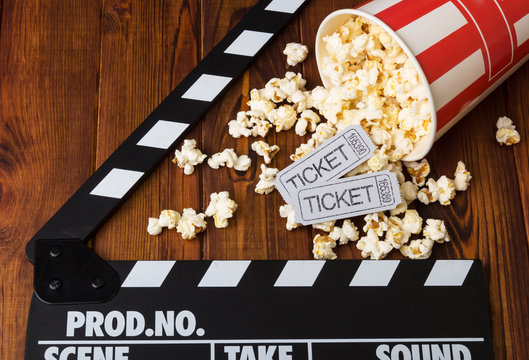 Spilled popcorn, striped box, movie tickets and movie clapper against dark wood.