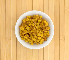Top view of a bowl of barbecue seasoned corn on a wood place mat.