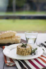 Risotto with asparagus in the ceramic plate over wooden table with silver fork, glass of water and colored striped tablecloth