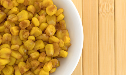 Top close view of a white bowl filled barbecue seasoned corn on a wood place mat.