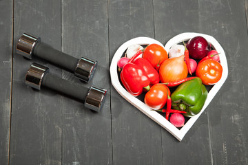 Sport and diet. Healthy lifestyle. Vegetables, dumbbells. Peppers, tomatoes, garlic, onion  radish in a heart on  black background