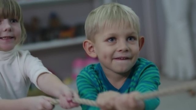 Closeup shot of little boy and girl excited about pulling the rope together in kids play room