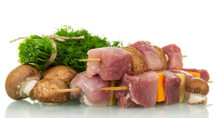 Pieces of raw pork, vegetables on wooden skewers and mushrooms, dill isolated on white.