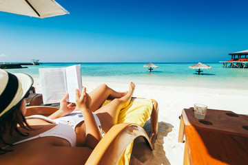 Woman on sunbed reading book under parasol at tropical island