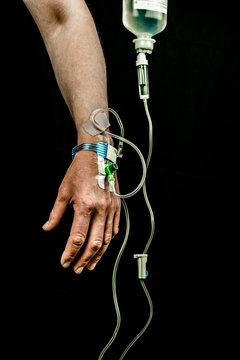 Hand and arm of patient with iv fluid treatment on black background, vertical.	