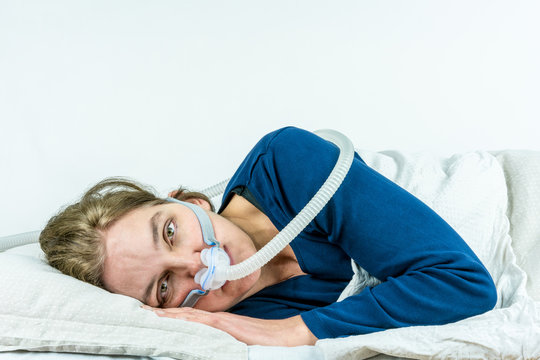 Woman laying on her side with eyes open looking in to camera. CPAP, sleep apnea treatment. Studio portrait white background.