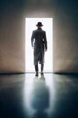 Man silhouette walking away in the light of opening door in dark room