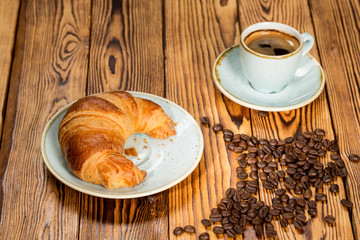 You want it. High angle shot of a delicious croissant and a cup of coffee surrounded by spilled roasted coffee beans on a cafe table.
