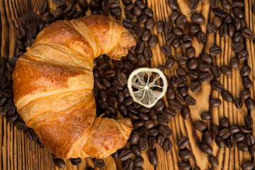True art. Shot of a croissant and a lemon slice lying on a table full of freshly roasted aromatic coffee beans.