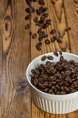 Waiting to be prepared. Shot of roasted coffee beans falling in to a bowl on a texture wooden table.