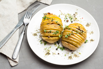 Potatoes baked with herbs on a white plate on a gray background.