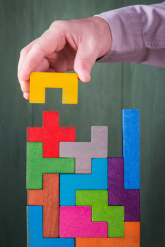 Hand with tetris toy blocks. Businessman builds a tower of wooden multi-colored blocks.  Concept of business success, cooperation, achievement.