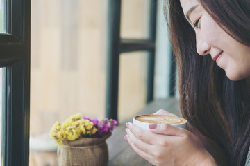 A beautiful asian woman holding and smelling hot coffee cup in loft cafe with feeling happy and smiley face