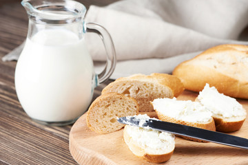 Sliced bread with creamy curd on wooden plank