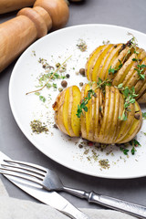 Baked potatoes with thyme on a plate, fork, knife salt shaker and pepper on a gray background.