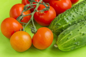 Red cherry tomatoes and green cucumbers on green cutting board.
