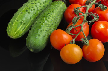 red tomatoes and green cucumbers on black background