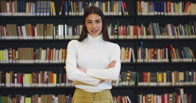 Portrait of a beautiful young woman smiling happy in a library holding books after doing a search and after studying. Concept: educational, portrait, library, and studious.