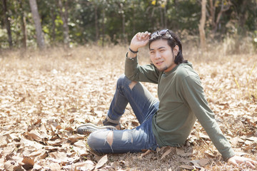 asian younger man sitting on dry leaves field with smiling face