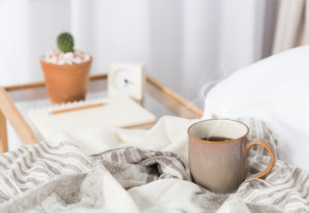 Cup of coffee on cozy white bed with cactus flowerpot,memo pat and alarm clock on wood bed side...