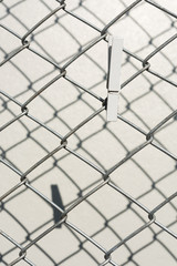 Fototapeta premium White wooden cloth pin over metal wire fence with shadow on cement wall backgroun