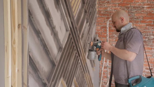 Bald man using a spray gun to paint the facade of the house. Specialist tests the size of the jet for spraying and adjusts power. The fingers of the person holding the handle of a special device. On