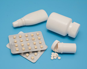 Pills and white bottles of medicine on a blue background. Medical theme and abstraction