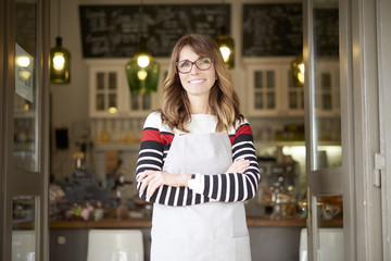 Proud small coffee shop owner businesswoman. Shot of  a happy barista woman standing at doorway and inviting to her coffee shop. Small business. 
