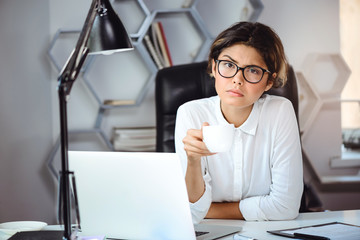 Young beautiful confident businesswoman drinking coffee at workplace in office.