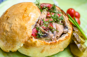 A roll stuffed with meat, tomatoes and herbs, pickled cucumbers and tomatoes on a green plate