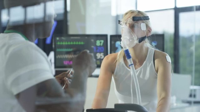  Female athlete on exercise bike being tested and monitored by sports scientist. 