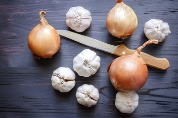 Onion, garlic and knife on a black wooden background