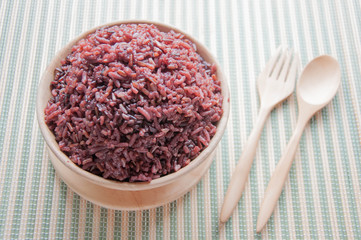 Obraz na płótnie Canvas Purple rice in a Wooden bowls, wooden spoons and wooden forks. Organic rice in a wooden bowl with spoon and fork on a green mat.
