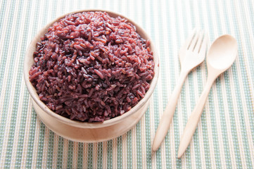 Purple rice in a Wooden bowls, wooden spoons and wooden forks. Organic rice in a wooden bowl with spoon and fork on a green mat.