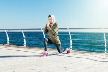 Sporty woman in the hood doing exercises on the coast in the spring