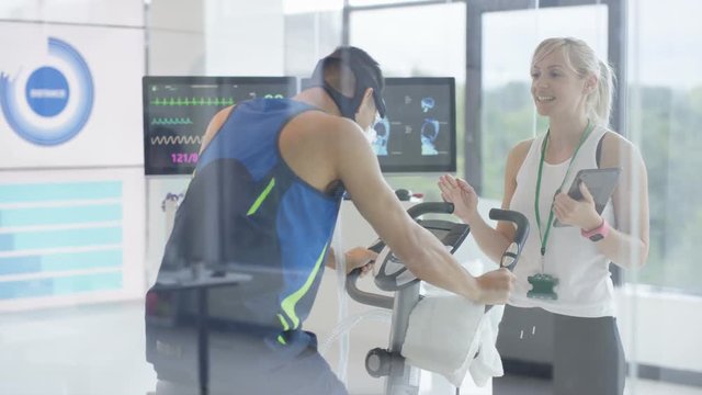  Man on exercise bike having fitness levels analyzed with hi tech equipment. Professional athlete in training, personal trainer at the gym or scientific research concept. 