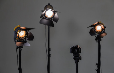 Digital SLR camera and three spotlights with Fresnel lenses. Manual interchangeable lens for filming. Shooting in the interior with artificial light. Equipment for movies.