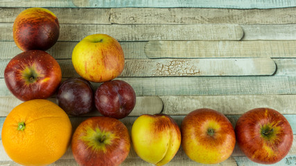 Red apples, nectarine, blue plums and orange on wooden table