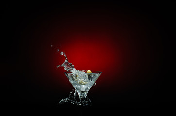 Olive splashing on cocktail isolated on red and black background