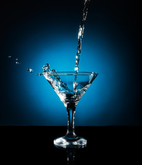 Splash from pouring martini into the glass. Object on a blue background