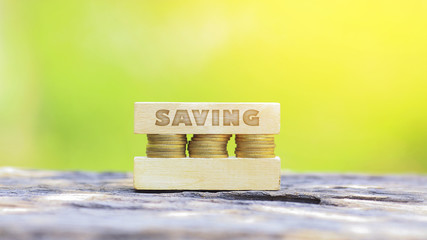 Business Concept - SAVING WORD, Golden coin stacked with wooden bar on shallow DOF green background