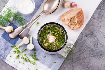 Cold Soup Okroshka in enamel cup and raw ingredients on grey stone table