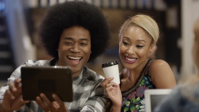  Happy young friends in city coffee shop pose to take a selfie with tablet
