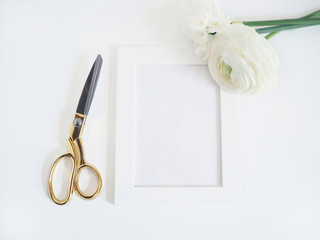 Styled stock photo. Feminine product mockup with bunch of buttercup, Ranunculus and daffodil flowers, blank white frame and golden scissors on white background. Flat lay, top view.