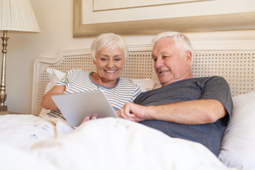 Smiling seniors using a digital tablet together in bed